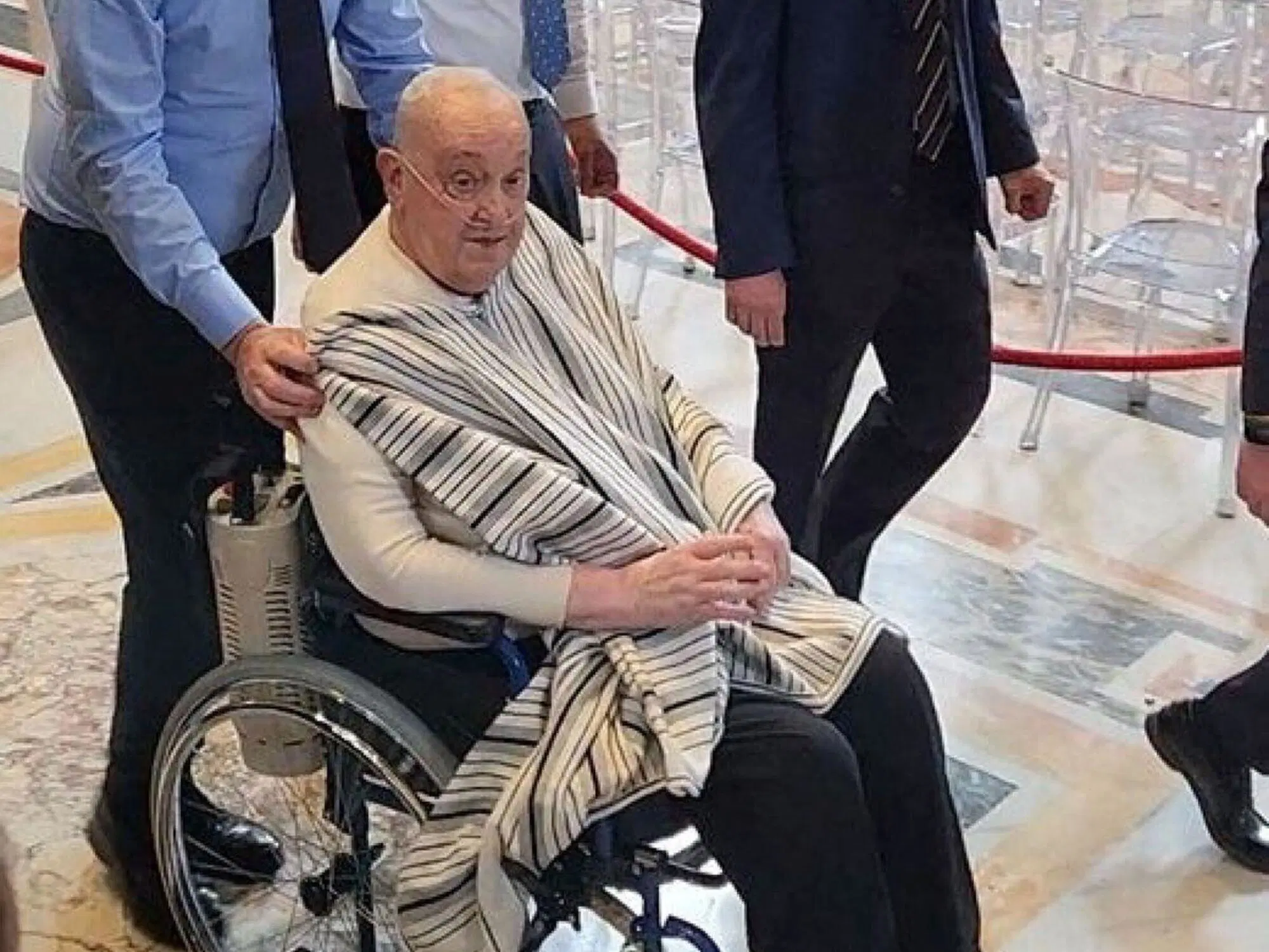 Bergoglio con il poncho-che-non-lo-era (come si vede &egrave; una coperta appoggiata e tenuta con la mano da chi spinge la sedia a rotelle)
