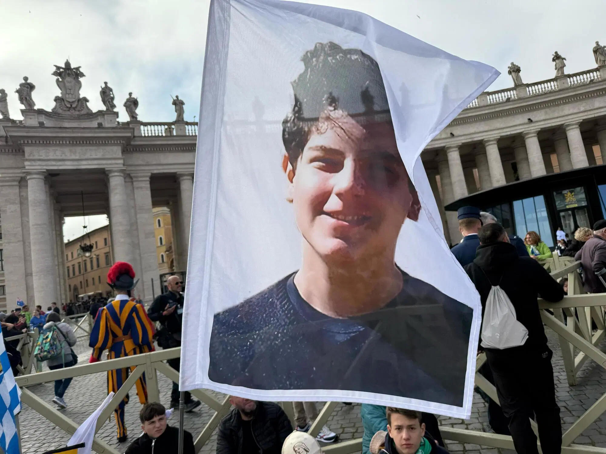 Dei ragazzi tedeschi a Piazza San Pietro con una bandiera di Carlo Acutis